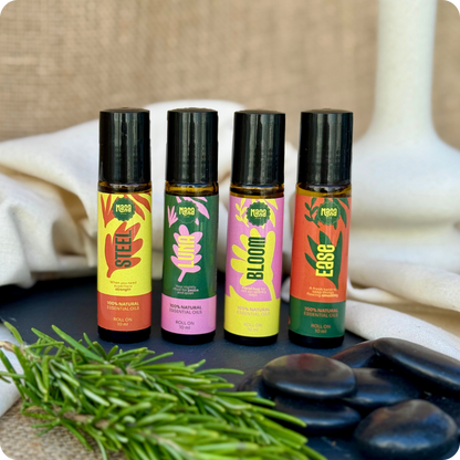 The four Manna aroma rollers arranged with rosemary sprigs and smooth dark stones