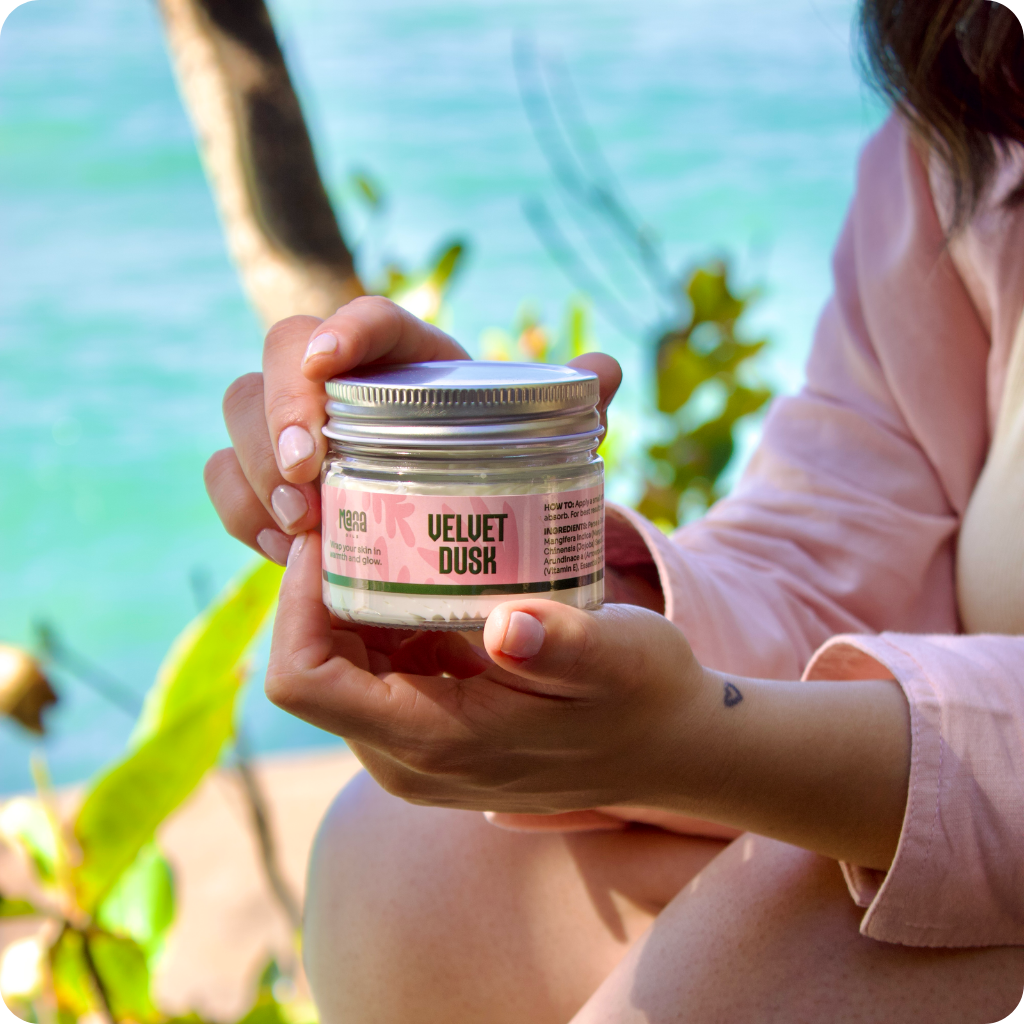 A jar of Velvet Dusk body butter held in both hands beside the water